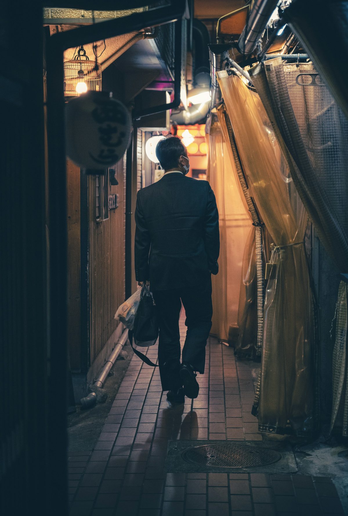 A man in a suit walking down a lantern-lit alley at night